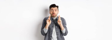 Umut dolu komik adam şans için nefes alıp dua ediyor, dilek tutuyor, haber bekliyor, somurtuyor ve kameraya bakıyor, beyaz arka planda duruyor..