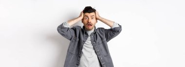 Telaşlı genç adam kameraya bakıyor, endişeli ve sıkıntılı görünüyor, büyük bir problemi var, beyaz arka planda panikliyor..