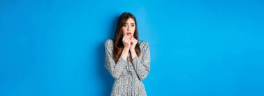 Korkmuş ve ürkek bir kadın, korkudan titriyor, nefes nefese göğsüne bastırılmış, korku filmi seyrediyor, mavi arka planda duruyor..