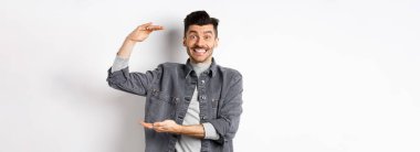 Neşeli adam gülümsüyor ve büyük boy gösteriyor, büyük bir şey gösteriyor ve heyecanlı görünüyor, beyaz arka planda duruyor..