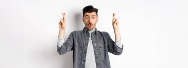 Heyecanlı genç adam şans dilemek ve nefes nefese kalmak için dua ediyor. Önemli haberleri bekliyor, yalvarıyor ya da dua ediyor, beyaz arka planda duruyor..