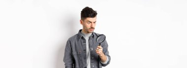 Ciddi araştırmacı, büyüteçle aşağı bakan, ciddi bakan, beyaz arka planda duran.