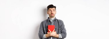 Aptal genç adam çekingen suratlı logoya bakıyor, günlüğünü göğsüne bastırıyor, günlük tutuyor, beyaz arka planda duruyor..