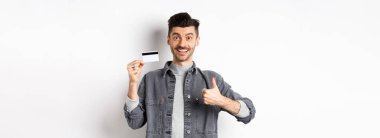 - Çok iyi. Plastik kredi kartı ile gülümseyen adam başparmağını kaldırıyor, gülümsüyor, bankayı tavsiye ediyor, beyaz arka planda duruyor..