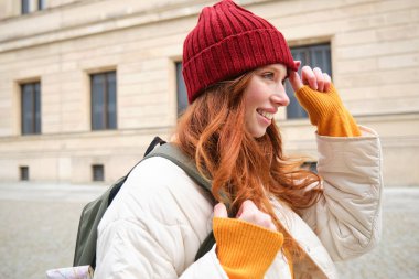 Tourism and travelling. Young redhead woman smiling, tourist walking with backpack around city centre, sightseeing, holds backpack with paper map.