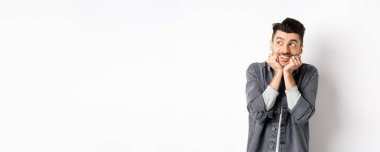 Heyecanlı genç adam sol üst köşede rüya gibi görünüyor, paketi bekliyor, hayal görüyor ya da hayal kuruyor, beyaz arka planda duruyor..