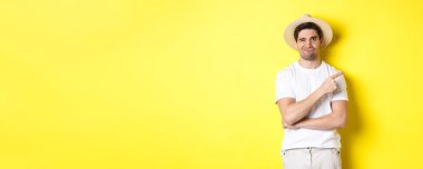 Şüpheci erkek turist şikayet ediyor, kötü ya da topal bir şeyi işaret ediyor, sarı arka planda eğlenmeden duruyor..