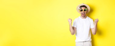 Mutlu adam tatile çıkıyor, kazanıyor ya da kutluyor, yaz şapkası ve güneş gözlüğü takıyor. Turist heyecanlı görünüyor, sarı arka planda duruyor..