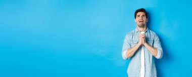 Çaresiz bir adam yardım için yalvarıyor, Tanrı 'ya yalvarıyor, el ele tutuşup dua ediyor, mavi arka plana karşı duruyor..