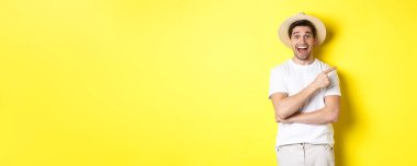 Hasır şapkalı mutlu erkek turist sağda, fotokopi alanında tanıtım teklifini gösteriyor, sarı arka planda. Boşluğu kopyala