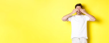 Mutlu adam gözlerini kapar ve şaşırmayı bekler. Gülümser, eğlenir, sarı arka planda durur..