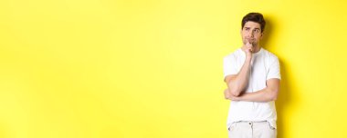 Genç erkek modelin portresi, sol üst köşeye bakıyor ve seçim yapıyor, fotokopi alanının yanında duruyor, sarı arkaplan.
