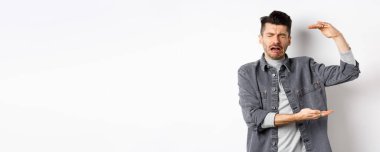 Üzgün adam ağlıyor ve büyük boy nesneler gösteriyor, büyük şeyleri şekillendiriyor ve şikayet ediyor, beyaz arka planda dururken hıçkırarak ağlıyor..