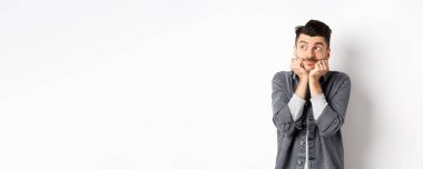 Heyecanlı genç adam sol üst köşede rüya gibi görünüyor, paketi bekliyor, hayal görüyor ya da hayal kuruyor, beyaz arka planda duruyor..