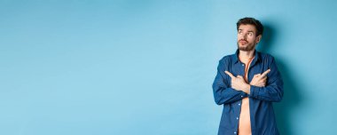 Kararsız sakallı adam çapraz kollar ve iki farklı türü gösteren, seçim yapan, mavi arka planda duran.