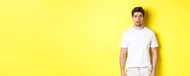 Kafası karışmış ve gergin bir adamın tuhaf bir şeye baktığı görüntüsü. Kaşlarını çatan, sarı arka planda duran..