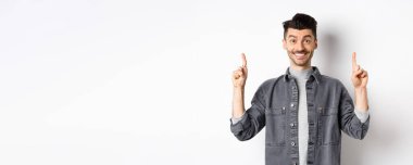 Heyecanlı genç adam gülümsüyor ve reklamını yapıyor, reklam teklifini işaret ediyor, beyaz arka planda duruyor..