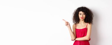 Kırmızı elbiseli ve makyajlı çekici bir bayan sol eli işaret ediyor, logoyu gösteriyor, beyaz arka planda duruyor..