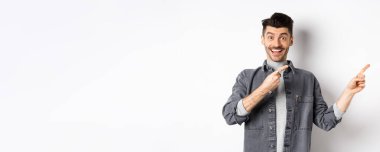 Bana bak. Mutlu stil sahibi bir adam gülümsüyor, parmaklarını boşluğa doğrultuyor, havalı tanıtım teklifleri sunuyor, beyaz arka planda kot ceket giyiyor..