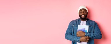 Not defteri tutan, gülümseyen, derslere çalışan, pembe arka planda duran yetişkin bir zenci resmi..