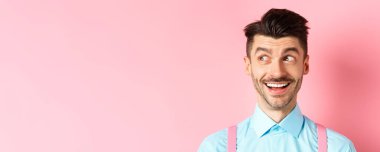 Neşeli gülümseyen adamın yakın çekimi, logoya bakıyor, heyecanlı yüzüyle reklam anlaşmasına bakıyor, pembe arka planda duruyor..