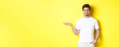 Kafası karışmış ve canı sıkkın adam elini kaldırsın, kafası karışmış, sarı arka plana karşı dursun. Boşluğu kopyala