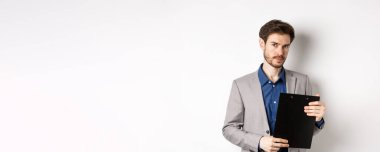 Genç erkek CEO elinde belgelerle pano tutuyor ve kameraya bakıyor, ofisi inceliyor, beyaz arka planda duruyor..