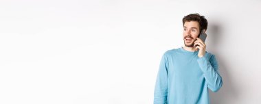 Teknoloji konsepti. Neşeli bir adam cep telefonuyla konuşuyor, telefonla konuşuyor ve eğleniyor gibi görünüyor, beyaz arka planda duruyor..