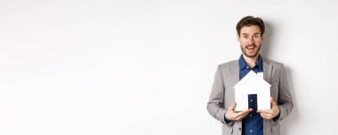 Gayrimenkul. Elinde kağıt ev kesimi, takım elbiseli ve kameraya umutlu bakan heyecanlı bir erkek girişimci..