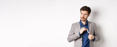 Kendine güveni tam ve başarılı bir iş adamı gibi görünen ve beyaz arka planda duran plastik kredi kartını takım elbisenin cebine koyan..