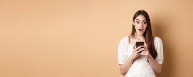 Telefonda heyecan verici haberler var. Şaşırmış genç bir kadın akıllı telefondan bej arka planda duran internet anonsunu okuduktan sonra....