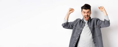 Motive olmuş genç adam bağırıyor ve ellerini kaldırıyor, maç seyrediyor ve takımı destekliyor, tezahürat yapıyor ve tezahürat yapıyor, beyaz arka planda duruyor..