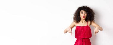 Kırmızı elbiseli etkileyici kadın diyor ki vay be, reklam anlaşması gösteriyor, parmaklarını şaşkın şaşkın aşağı gösteriyor, beyaz arka planda duruyor..