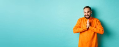 Mutlu adam teşekkür ediyor, el ele tutuşup dua ediyor, minnettar görünüyor ve gülümsüyor, açık mavi arka planda duruyor..