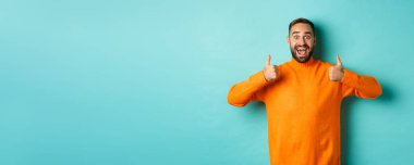 Hayret verici bir adam açık mavi arka planda duran harika bir şeyi onaylıyor ve övüyor..