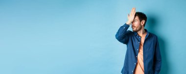 Sinirli ve yorgun adam facepalm, gözlerini devirme ve mavi arka planda duran aptal davranışlardan rahatsız olmuş görünme..