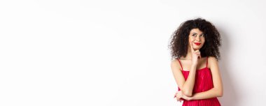 Kırmızı elbiseli zarif bir kadın resmi, düşünceli ve gülümseyen, romantik randevuyu düşünen, beyaz arka planda duran.