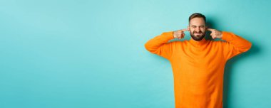 Hoşnut olmayan adam kulaklarını kapattı ve suratını buruşturan, gürültücü komşular, gürültüden rahatsız, açık mavi arka plan.