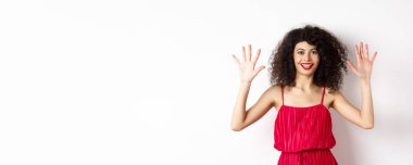 Kıvırcık saçlı, kırmızı elbiseli, on numarayı parmaklarıyla gösteren, beyaz arka planda duran güzel bir manken..