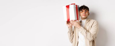 Hediye kutusunun içinde ne olduğunu dinleyen, tahmin etmeye çalışan, beyaz arka plana odaklanmış ilginç bir adam..