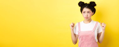 Çekingen, somurtan, dişlerini sıkan, kızgın ama sol üst köşede sevimli görünen, sarı arka planda makyajlı bir kız..