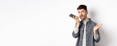 Havalı yakışıklı adam hoparlörden konuşuyor, dudak kenarındaki akıllı telefonla sesli mesaj kaydediyor, bir şeyleri tartışıyor ve beyaz arka planda duran boş alana bakıyor..