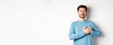 Kafkas sakallı genç bir adamın portresi elleri kalbi kapalı, gözleri kapalı, mutlu anların hayalini kuruyor, beyaz arka planda duruyor..