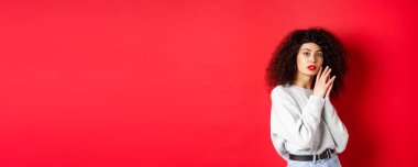 Kıvırcık saçlı, kırmızı dudaklı, yüzü makyajlı, kırmızı arka planda duran şehvetli ve romantik kız..