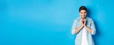 Komik kurnaz bir adam şeytani bir plan yapıyor, bir şeyler planlıyor ve gülümsüyor, mavi arka plana karşı duruyor..