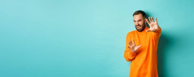 Tiksinmiş adam korunmak için el pençe divan durur, merhamet için yalvarır, nefretle dolu bir şeye bakar, açık mavi arka planda durur..