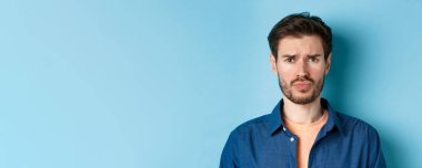 Üzgün ve gücenmiş genç bir adamın birine somurtması, üzgün olması, mavi arka planda durması..