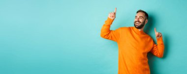 Yakışıklı adam kutlama yapıyor, kazandığını hissediyor, parmaklarını havaya kaldırıyor ve açık mavi arka planda dans ediyor..