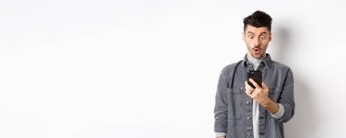 Adam akıllı telefon ekranına şaşırmış görünüyor, telefonda heyecan verici haberler alıyor, beyaz arka planda duruyor..