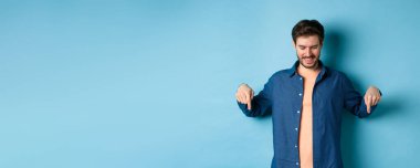 Sakallı, gülümseyen yakışıklı adam, pankarta bakıyor ve işaret ediyor, özel teklifi kontrol ediyor, mavi arka planda duruyor..